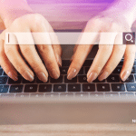 Picture of a woman's hands with light brown painted fingernails on a MacBook keyboard with a search engine search bar overlayed. Image is being used for a Newswire blog about SEO and press release distribution.