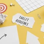 "Target Audience" is written on a scrap of paper on a yellow table top with other pieces of paper