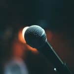 Close-up picture of a microphone on stage. Image is being used for a blog post titled, "How Are Small and Midsize Companies Using this Marketing Strategy to Amplify Messaging?"