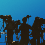 Shadows of media personnel with cameras on a blue backdrop. Image is being used for a Newswire blog about handling negative publicity.