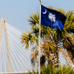 Picture of the South Carolina state flag and palm tree in front of the Arthur Ravenel Jr. Bridge. Image is being used for a Newswire blog post about the top media outlets in South Carolina