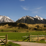 Picture of a ranch in Montana. Blue skies and a mountain range in the background. Image is being used for a Newswire blog post about the Top Media Outlets in Montana.