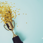 Picture of a trophy with gold confetti coming out of it on a blue background. Newswire branded image.