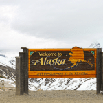 Picture of "Welcome to Alaska" sign with snow and gray clouds in the background. Image is used for a Newswire blog post about the top media outlets in Alaska.