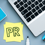 Picture of a computer with a yellow Post-It note next to it that says "PR." This image is being used for a Newswire blog post about PR services.