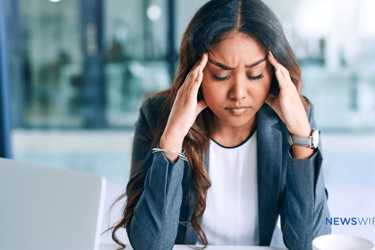 Picture of a business woman with dark complexion looking stressed and holding her hands at her temples. This image is being used for a blog about the use of media monitoring for crisis management.