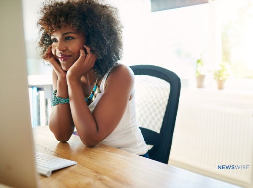 African American woman sitting in front of her computer with her head in her hands and a smile on her face.